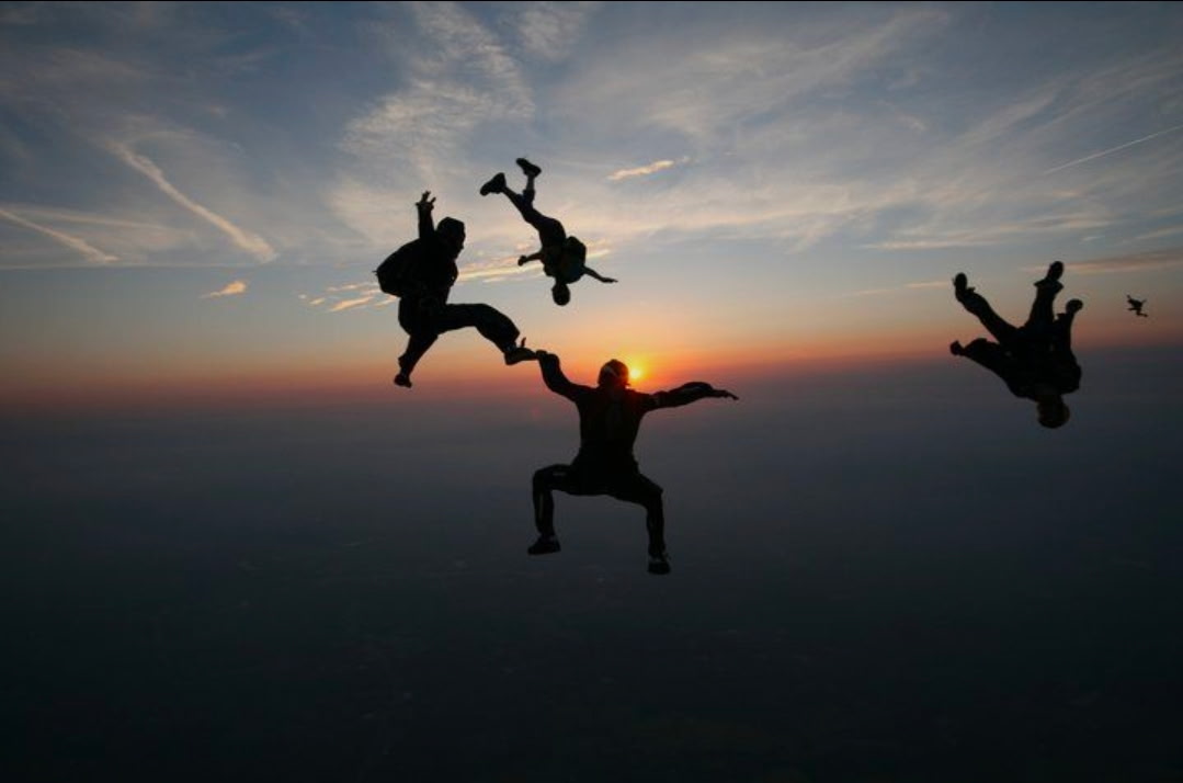 A group of skydivers in freefall with a sunset on the horizon